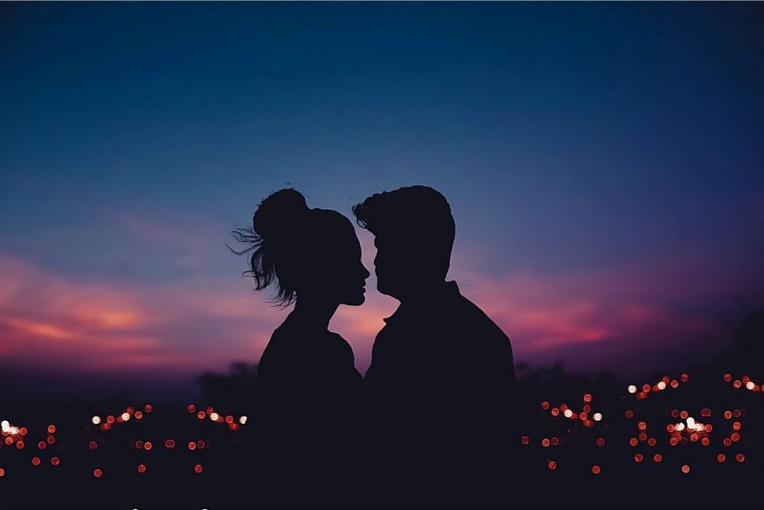 A couple standing over the city, looking like they are about to kiss.